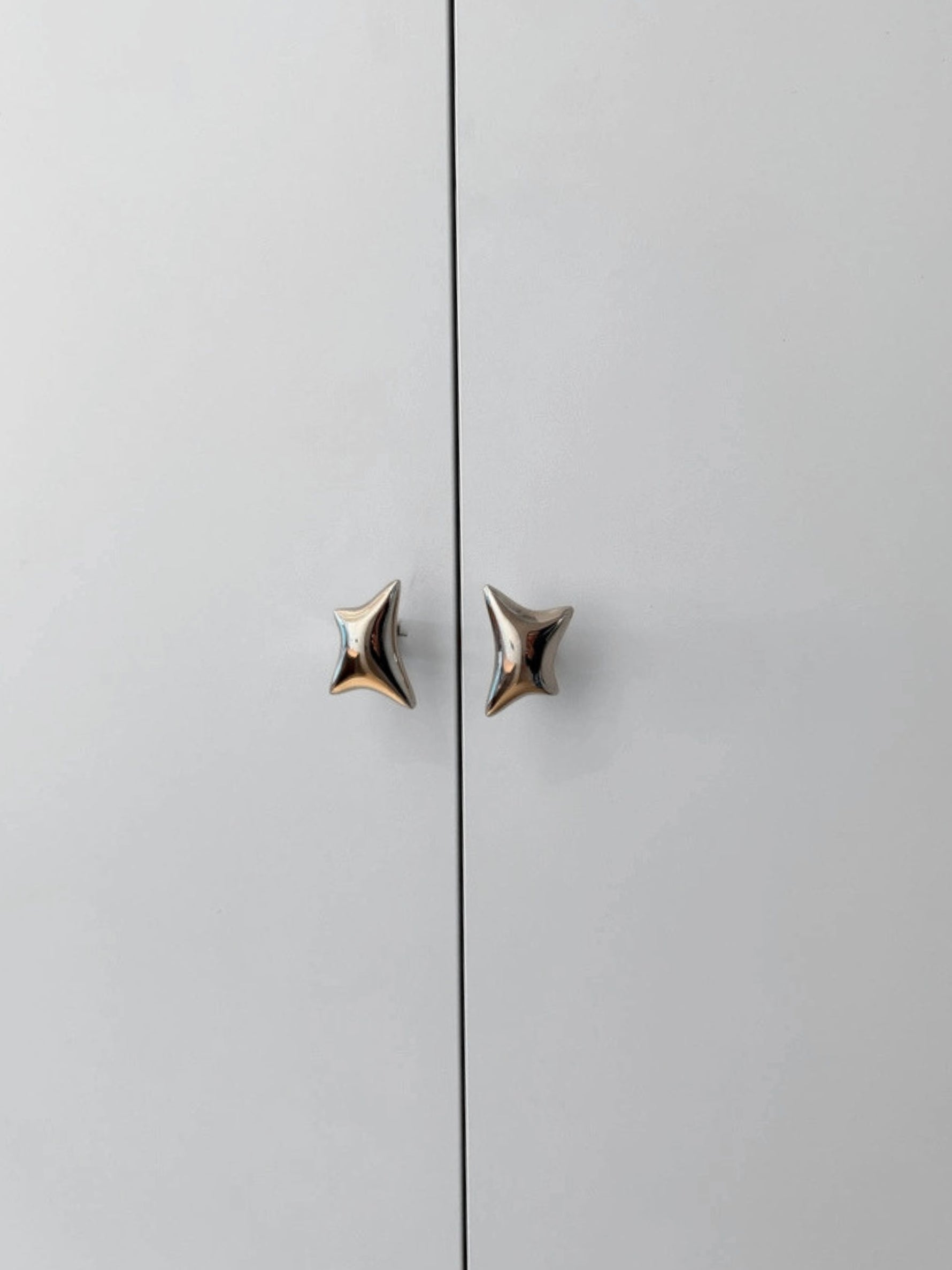 Two polished chrome wave star knobs mounted on light grey cabinet doors