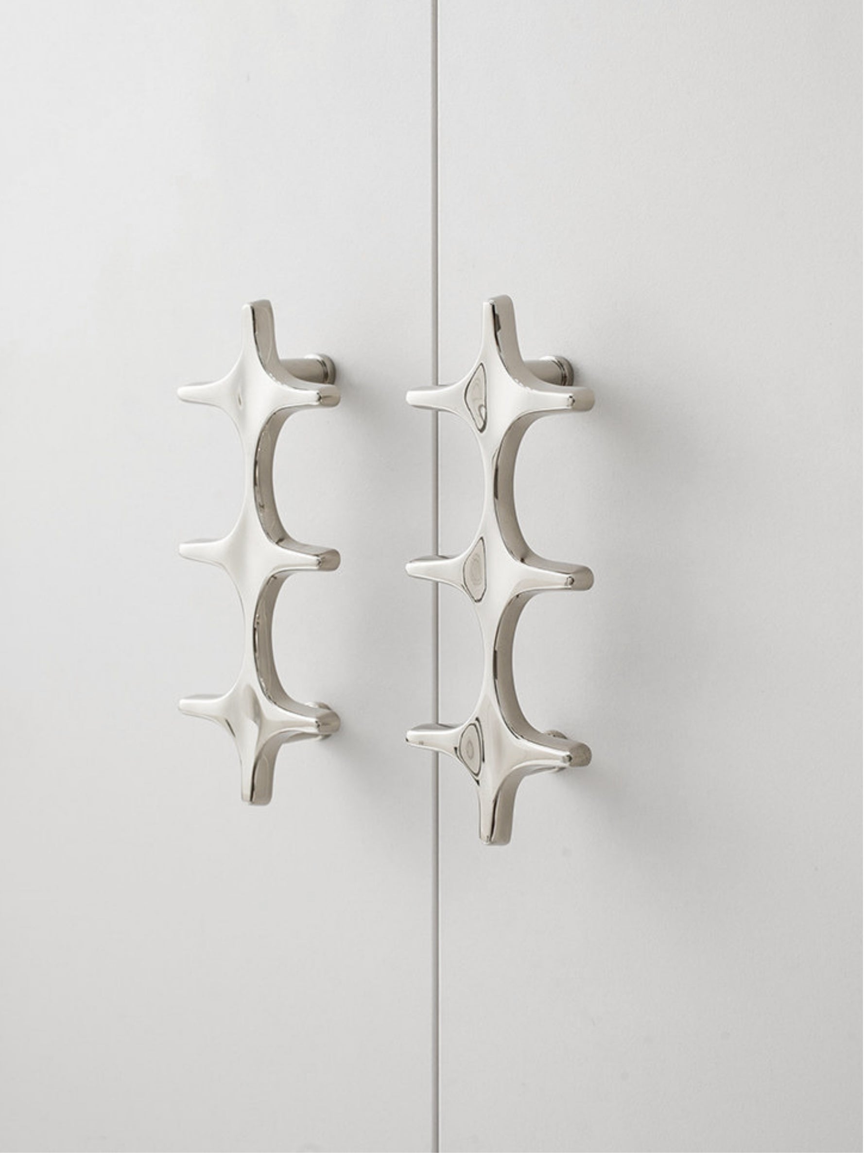 Close-up polished chrome star cross pulls on white cabinet doors with visible screws