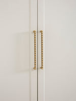 Close-up of a white cabinet with antique brass beaded handles on a light beige background