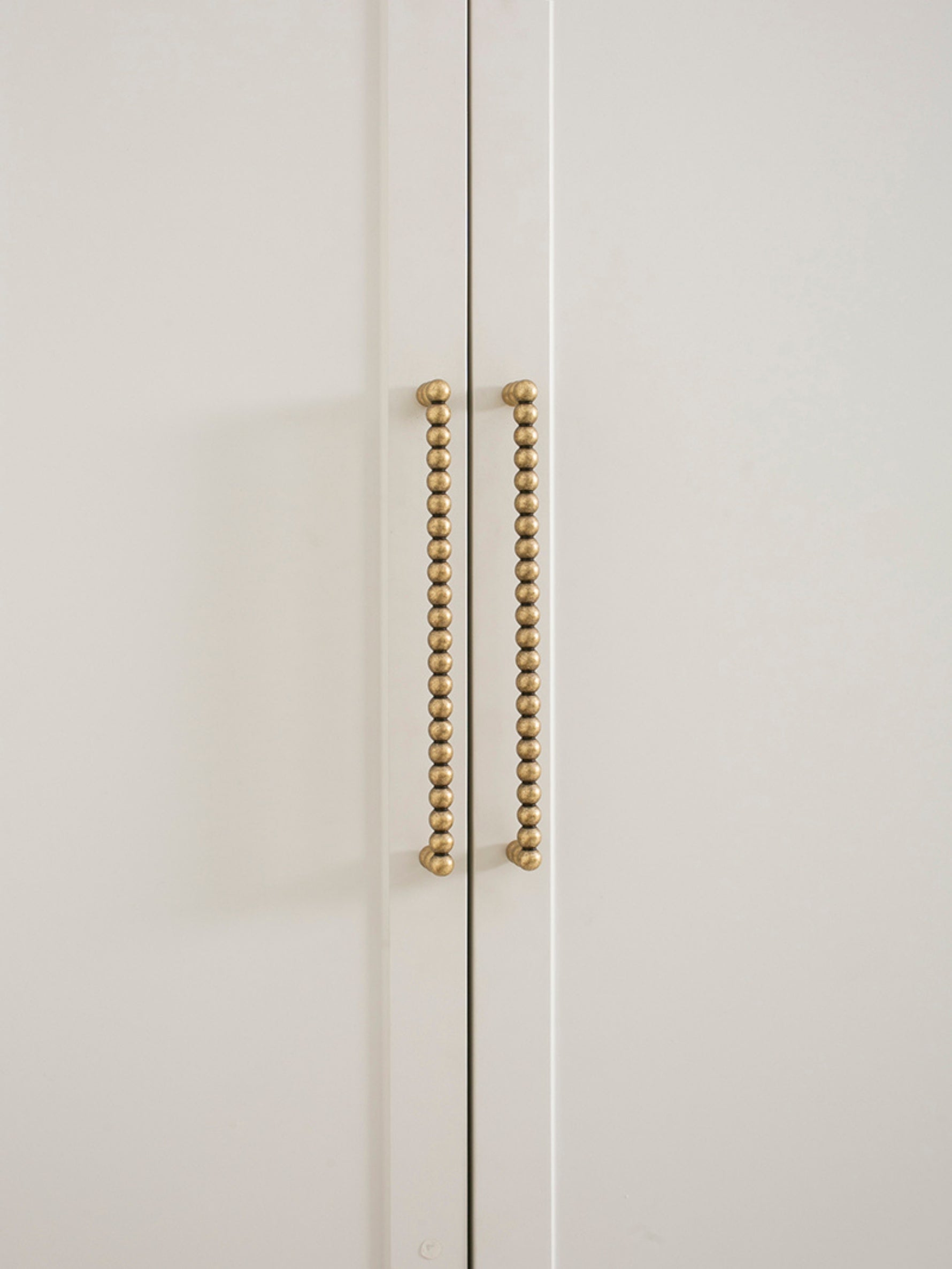 Close-up of a white cabinet with antique brass beaded handles on a light beige background