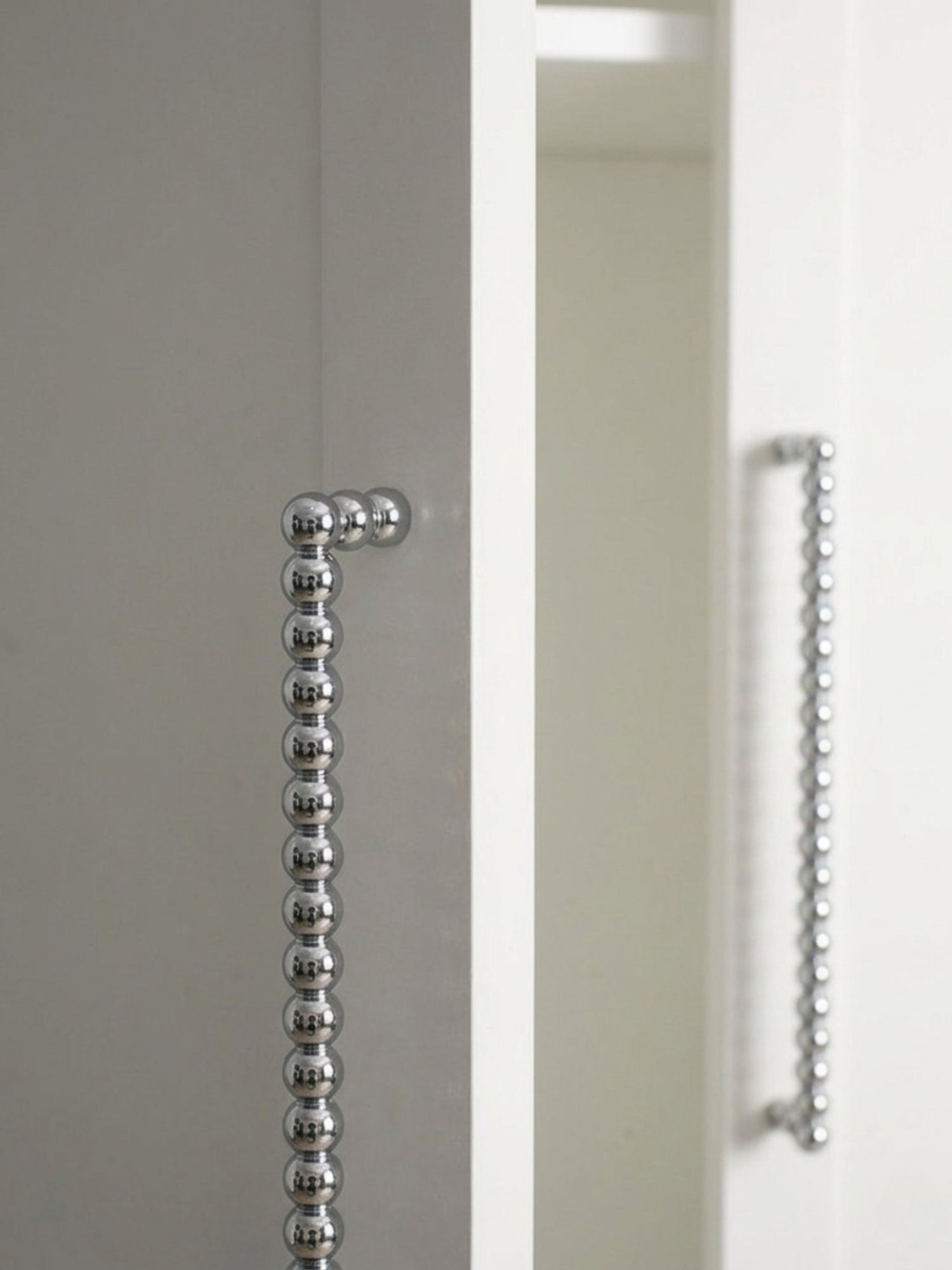 Close-up polished chrome beaded ball pull on grey and white cabinet edge showing bead detail
