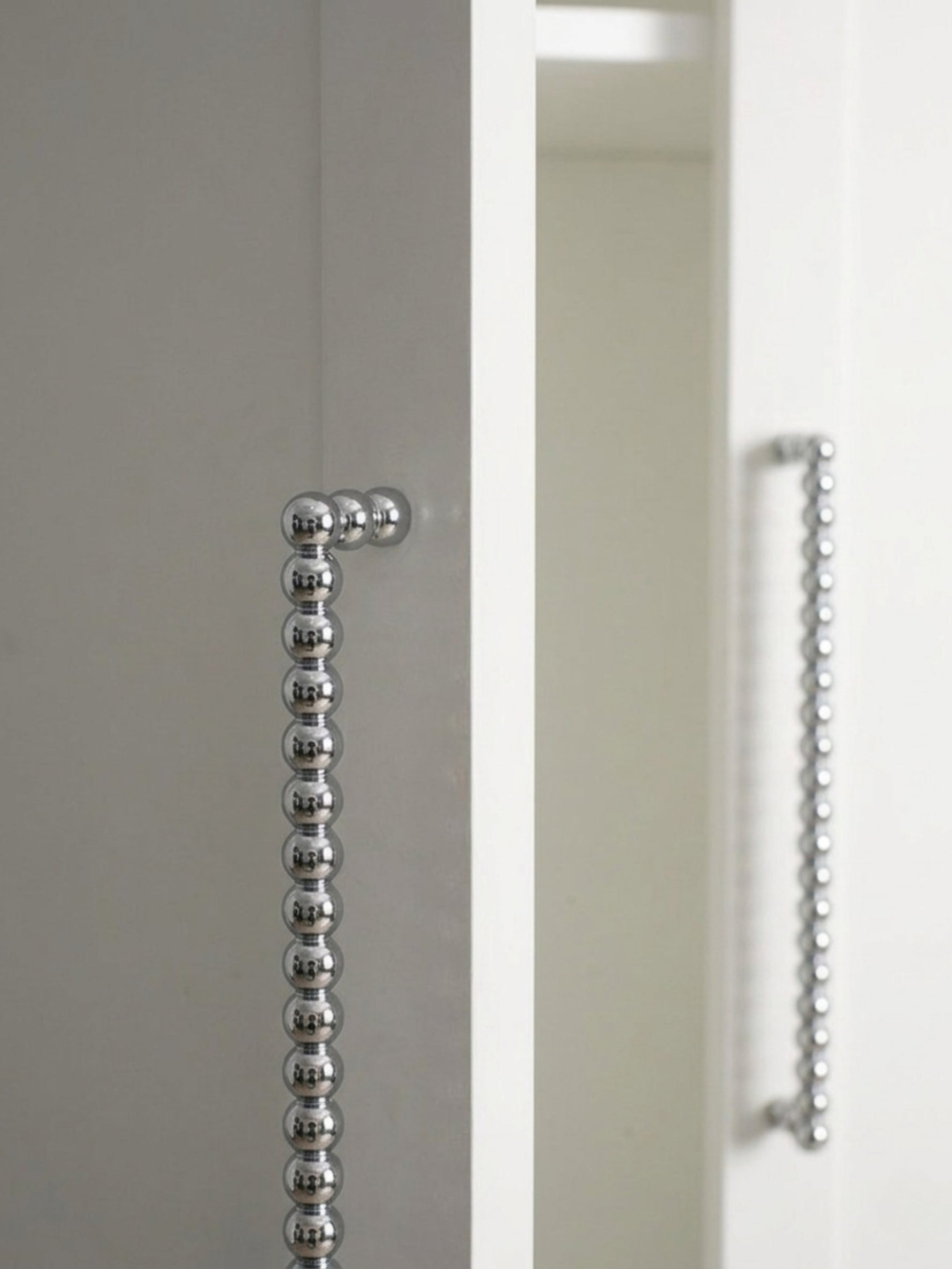Close-up polished chrome beaded ball pull on grey and white cabinet edge showing bead detail