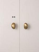 Size B brushed brass pebble knobs on white cabinet door
