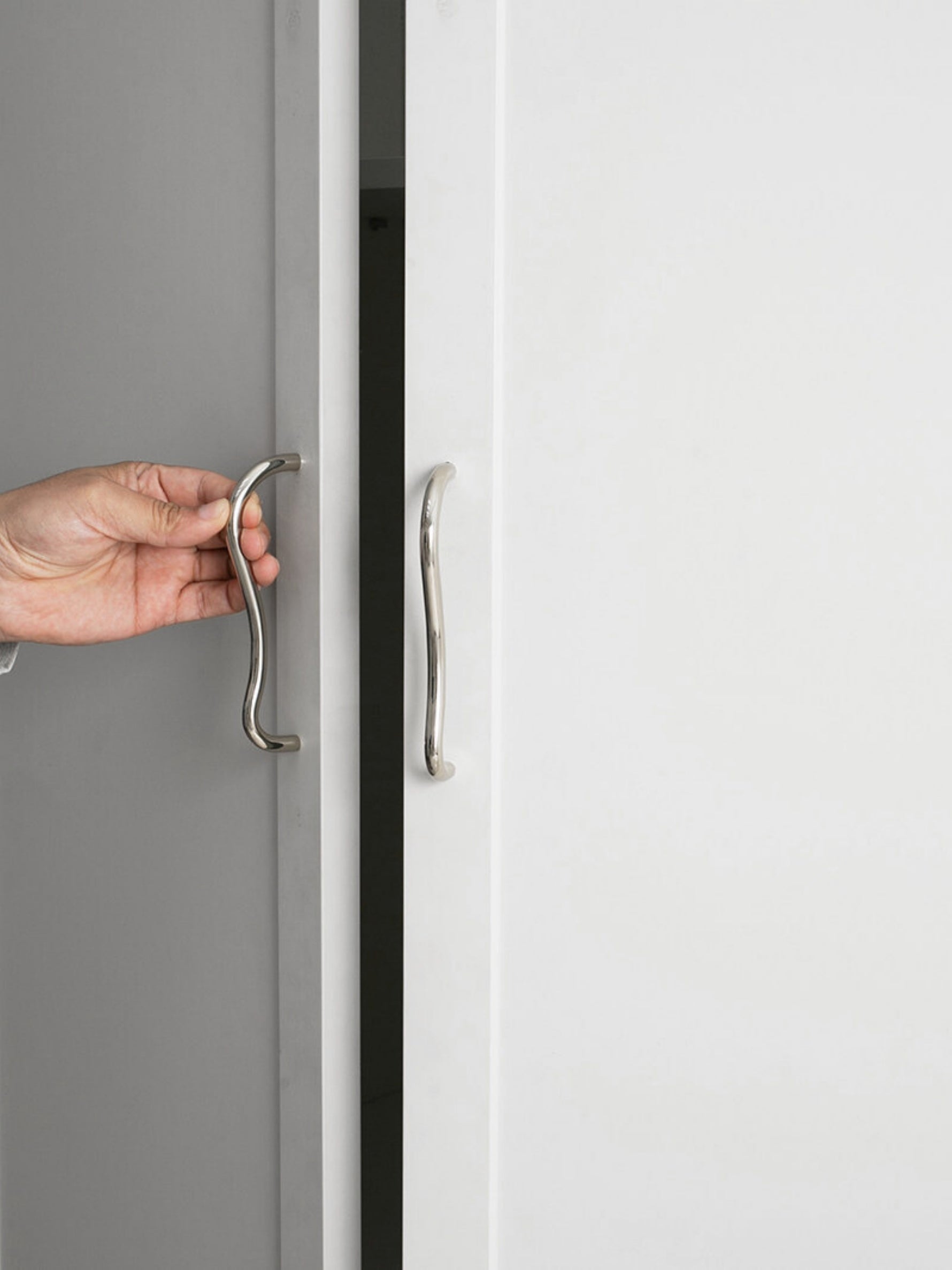 Close-up hand grip on chrome wave cabinet pull