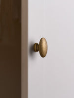 Antique brass oval cabinet knob on white cabinet door, edge view