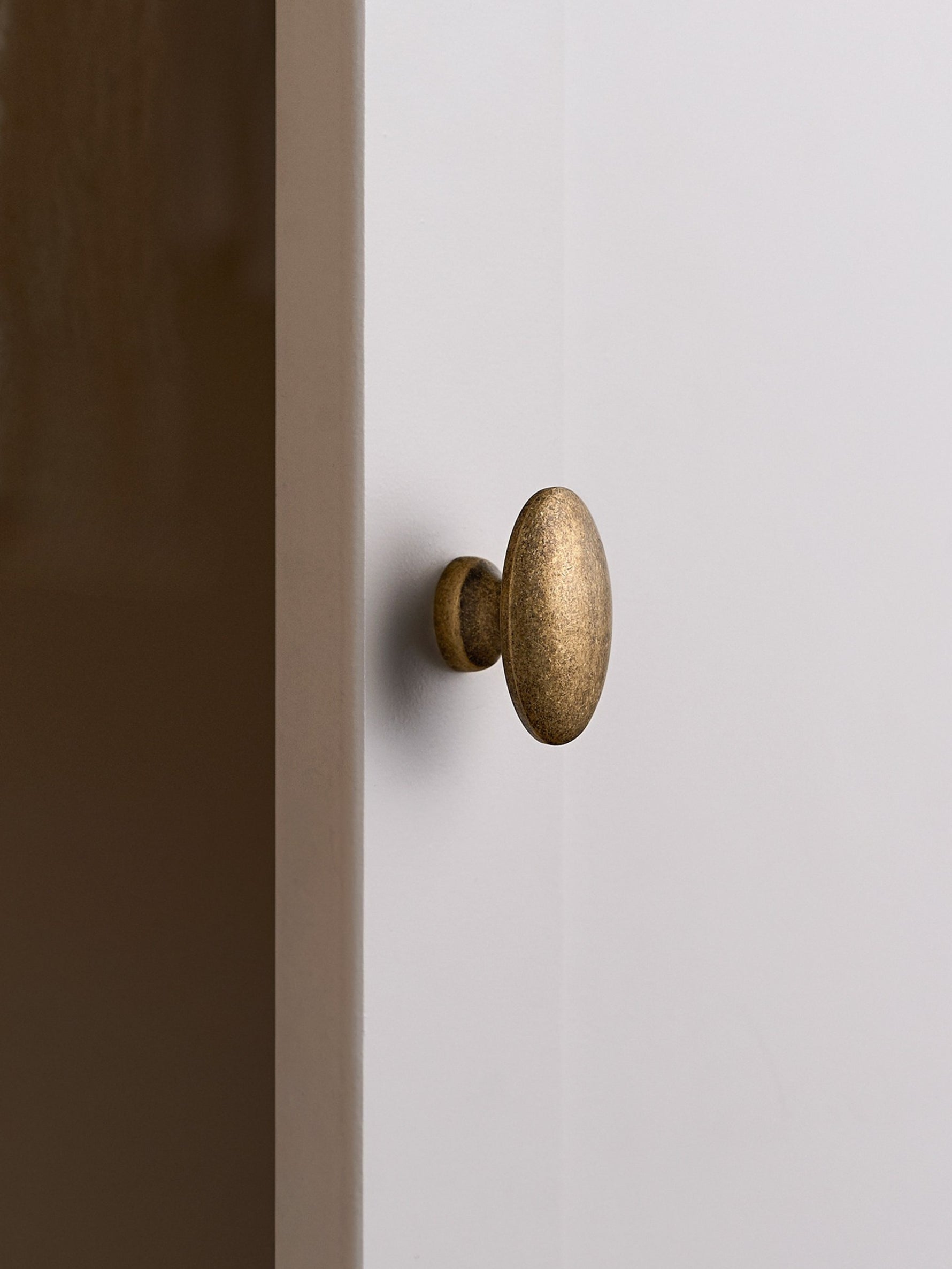 Antique brass oval cabinet knob on white cabinet door, edge view