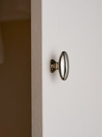 Nickel silver oval cabinet knob mounted on white cabinet door, edge view