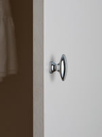 Polished chrome oval cabinet knob on white cabinet door, edge view