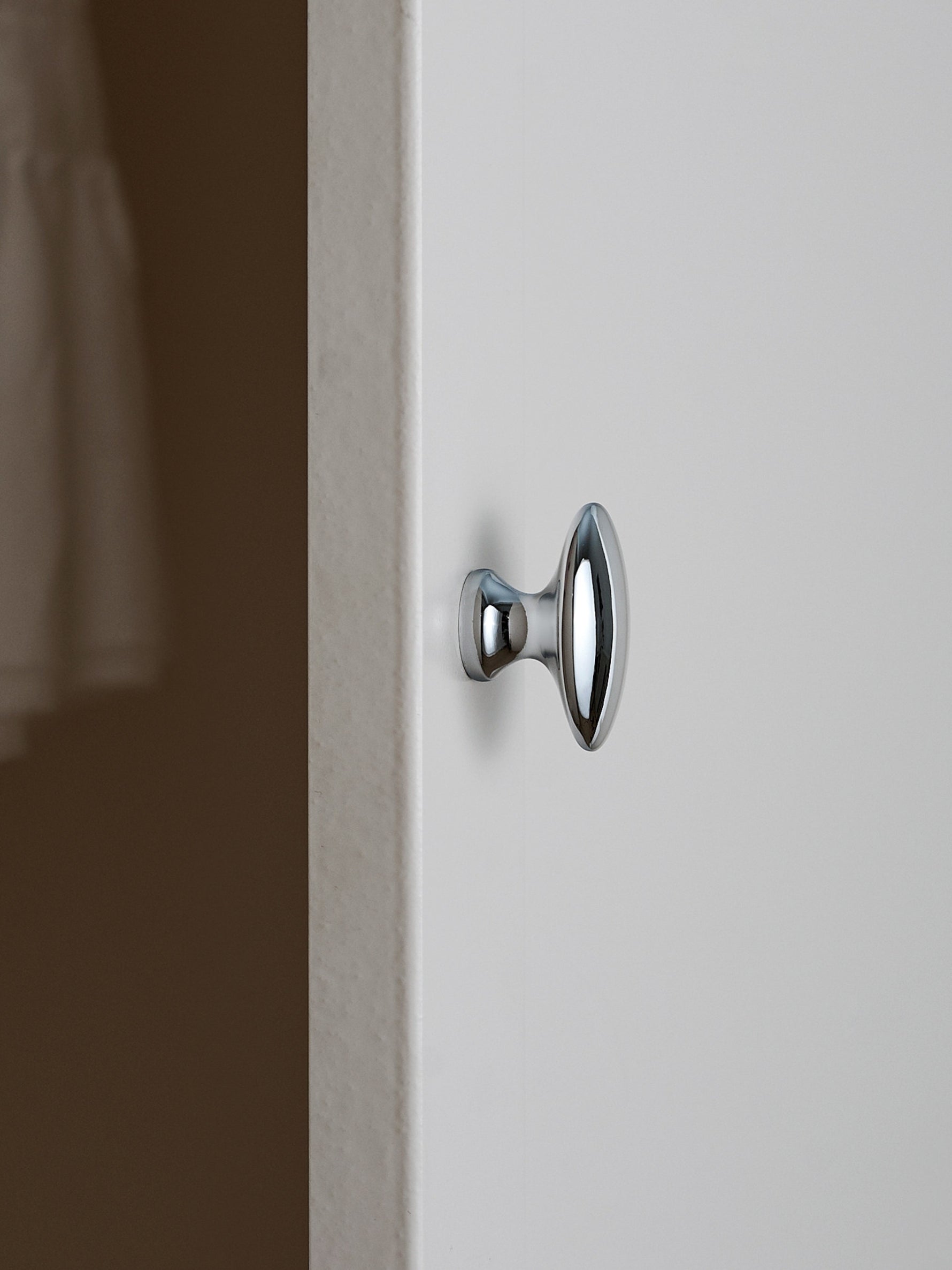 Polished chrome oval cabinet knob on white cabinet door, edge view