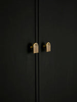 Solid brass Art Deco arch knob on black cabinet door, warm antique brass tone