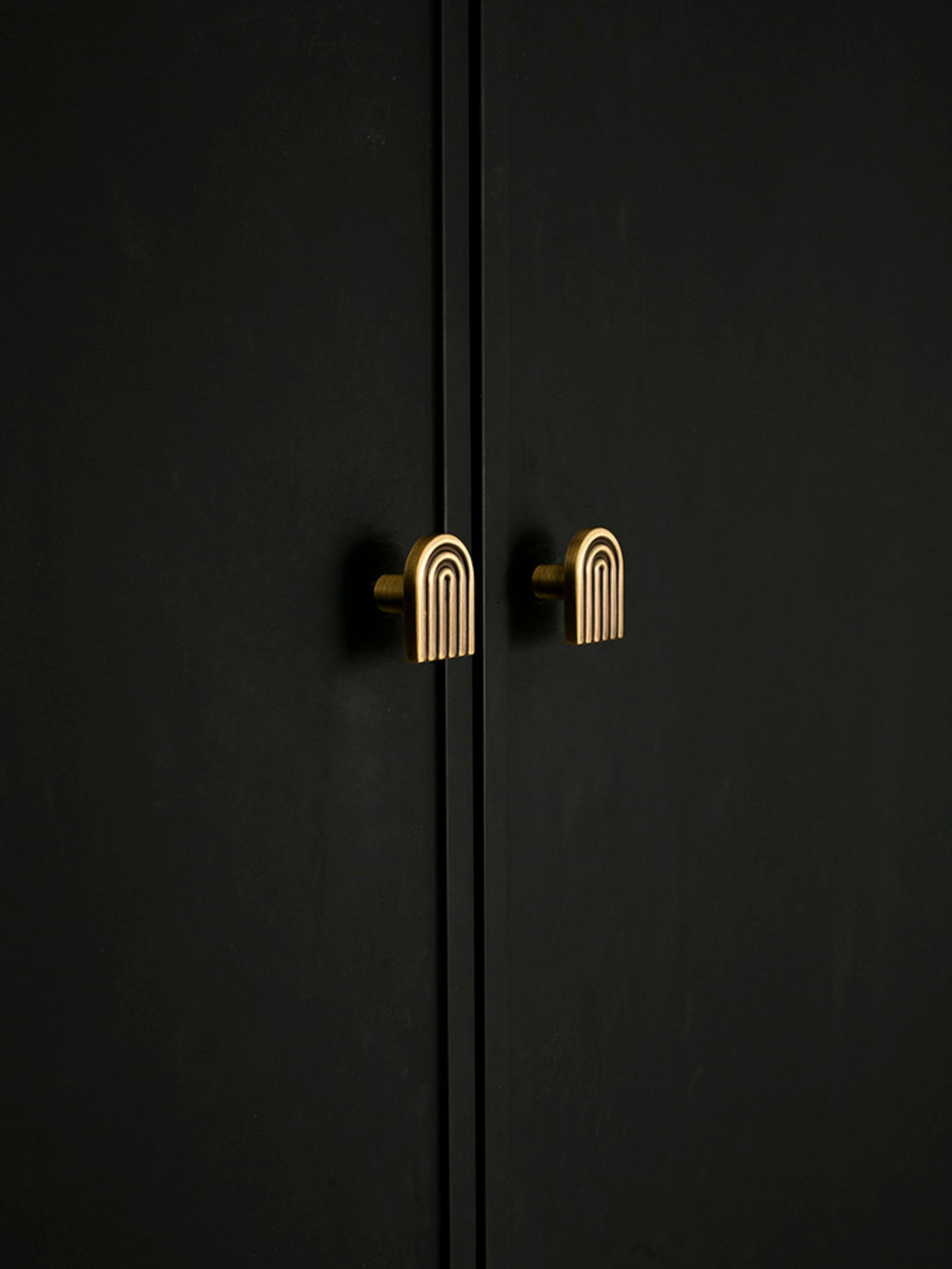 Solid brass Art Deco arch knob on black cabinet door, warm antique brass tone
