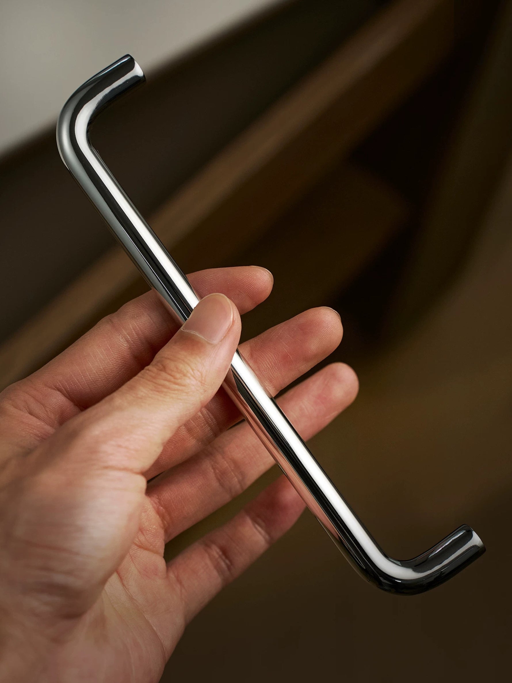 Polished chrome bar cabinet pull held in hand, showing profile