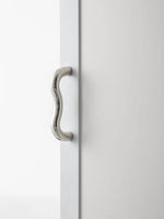 Polished chrome wavy S-curve pull on white cabinet door, full vertical view