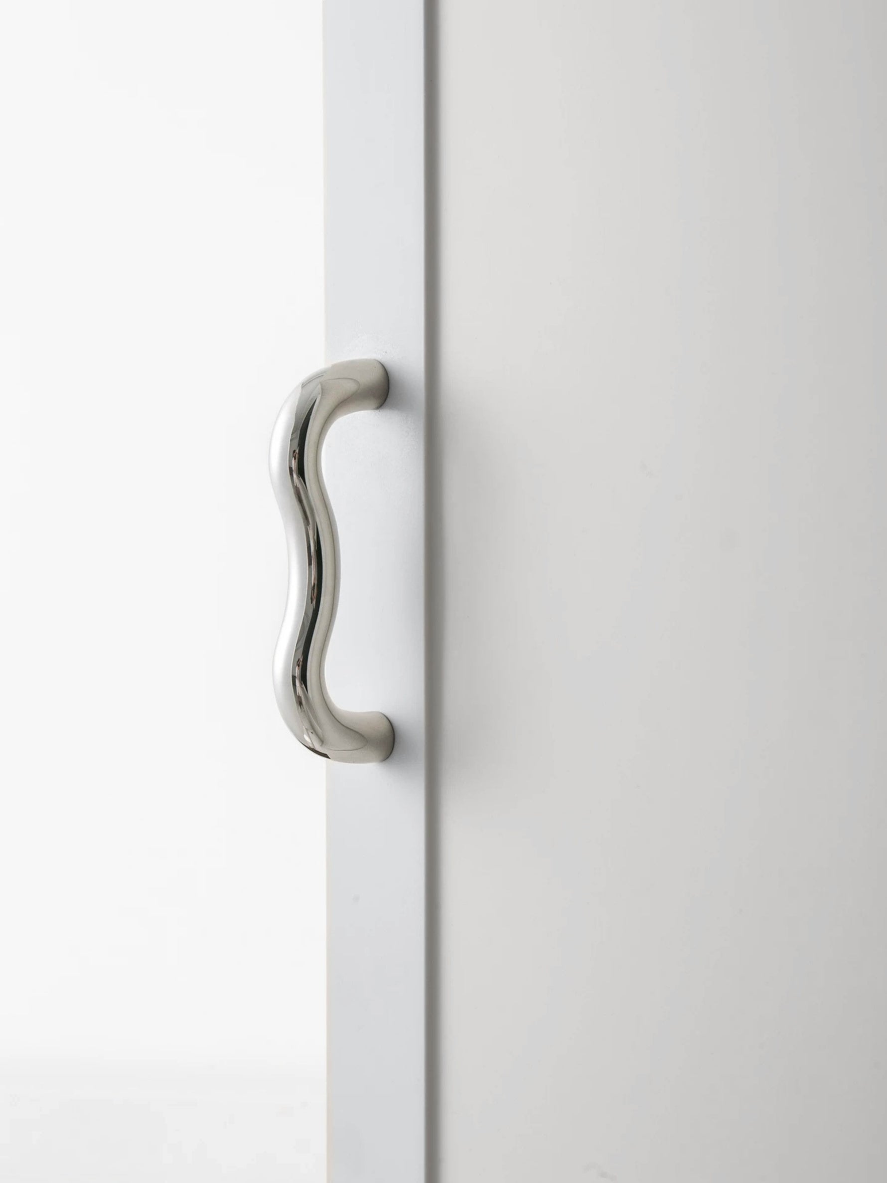 Polished chrome wavy S-curve pull on white cabinet door, full vertical view