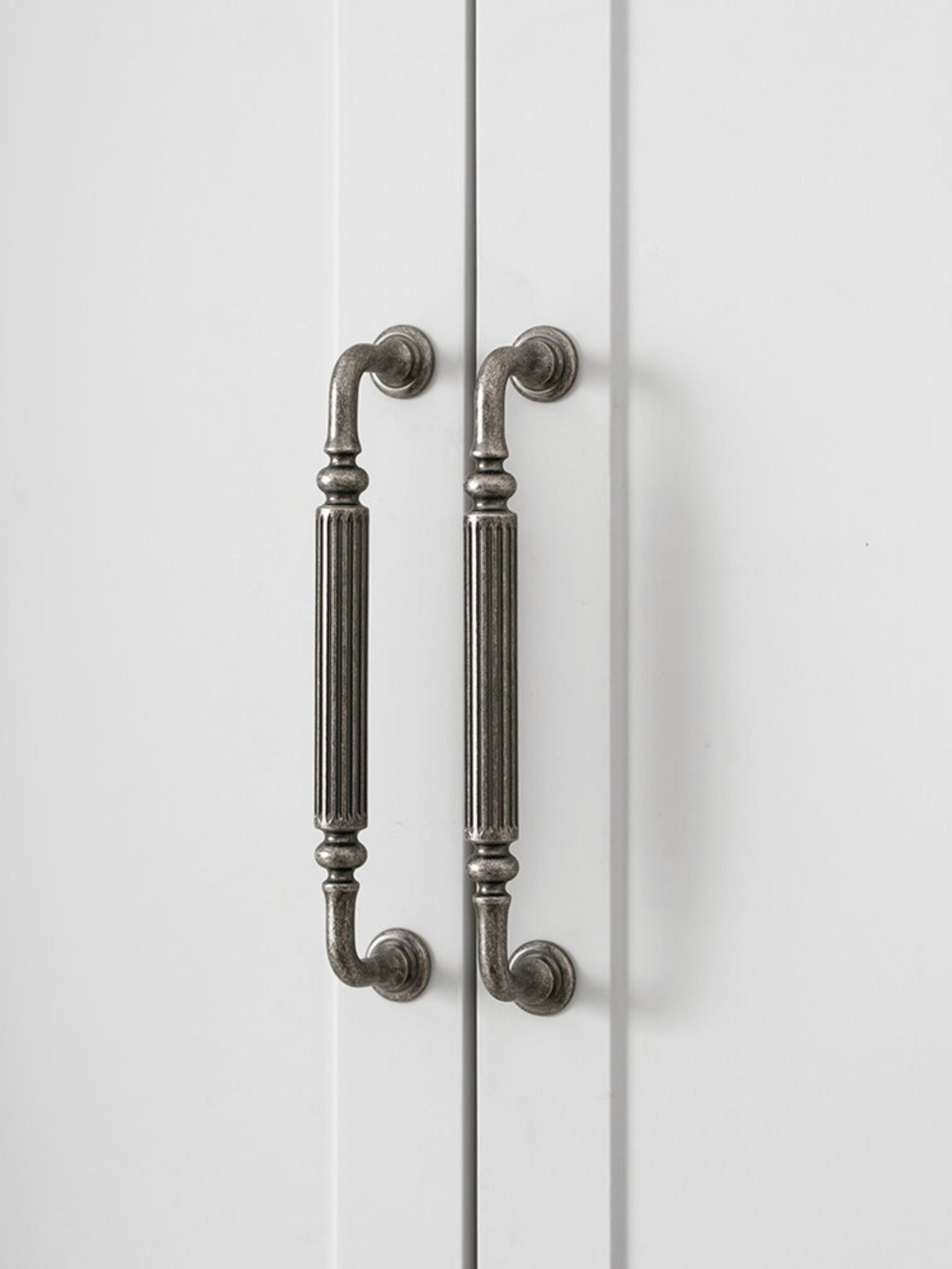 Two antique silver reeded cabinet pulls on white wardrobe doors, vertical