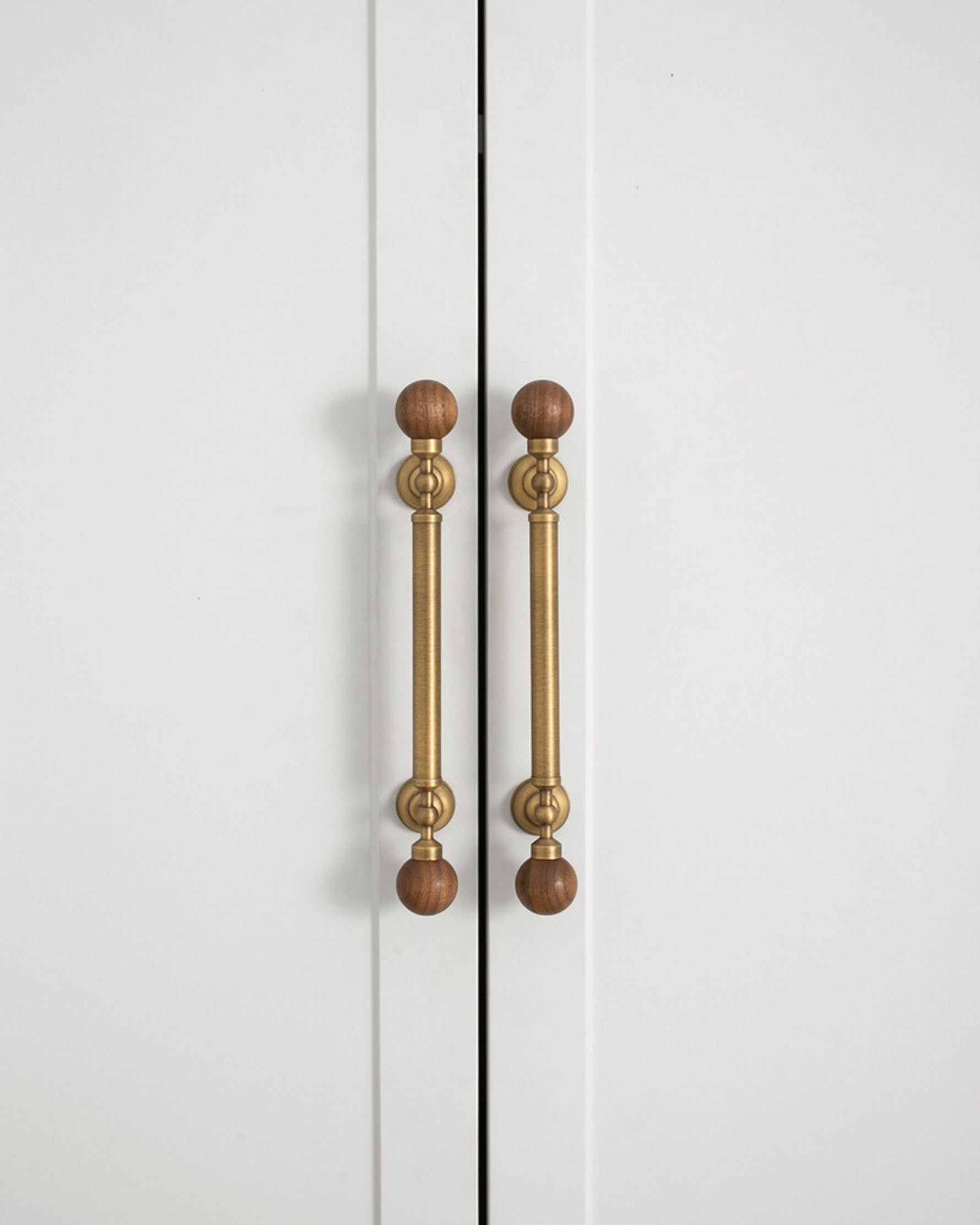 Walnut ball pulls on white wardrobe doors — vertical orientation