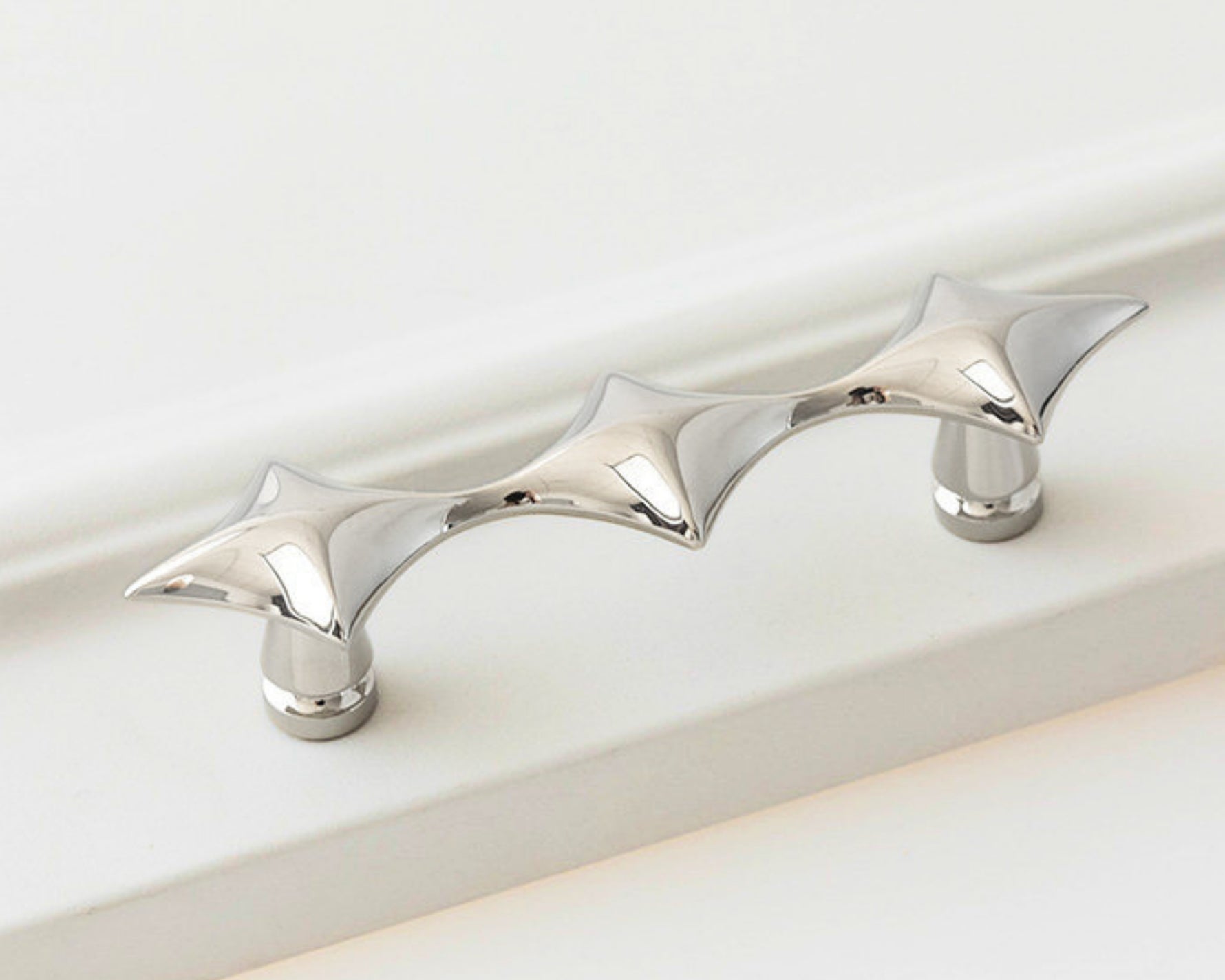 Polished chrome star cabinet pull on white surface, horizontal close-up
