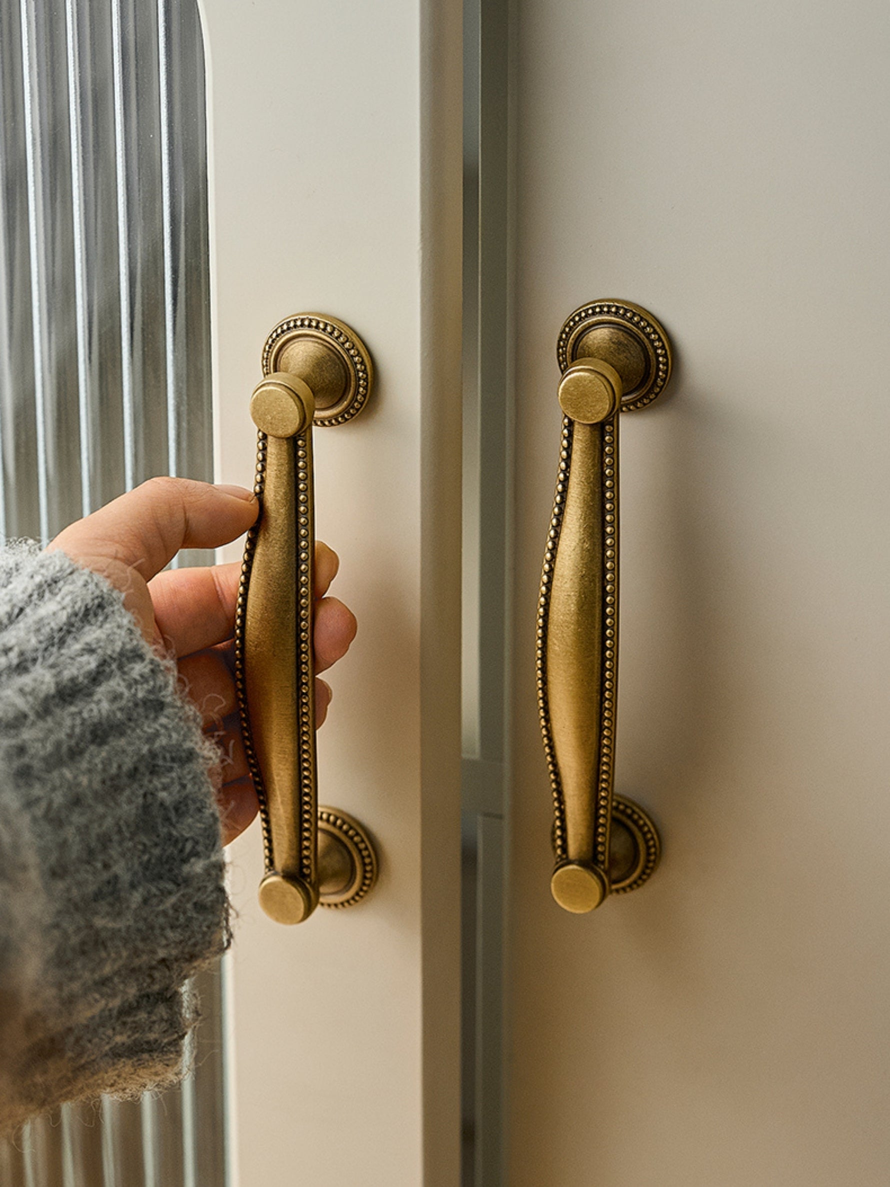 Hand holding antique brass beaded bar pull on cream wardrobe door
