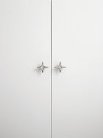 Two polished chrome star knobs on white wardrobe doors, front view