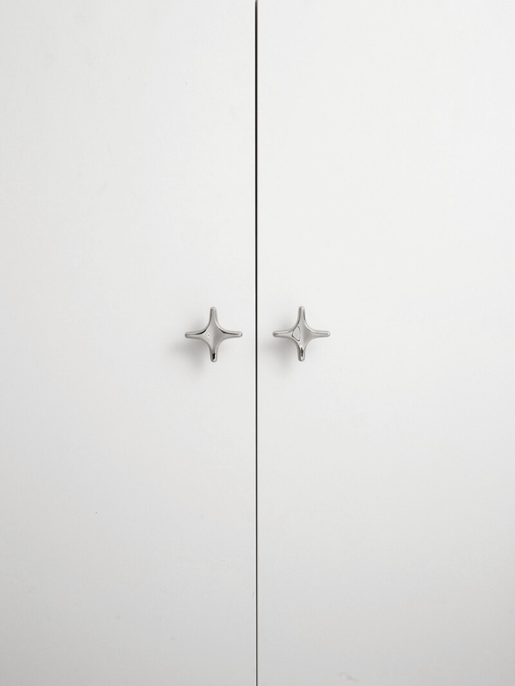 Two polished chrome star knobs on white wardrobe doors, front view