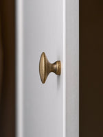 Antique brass oval cabinet knob on white door, profile view showing pedestal