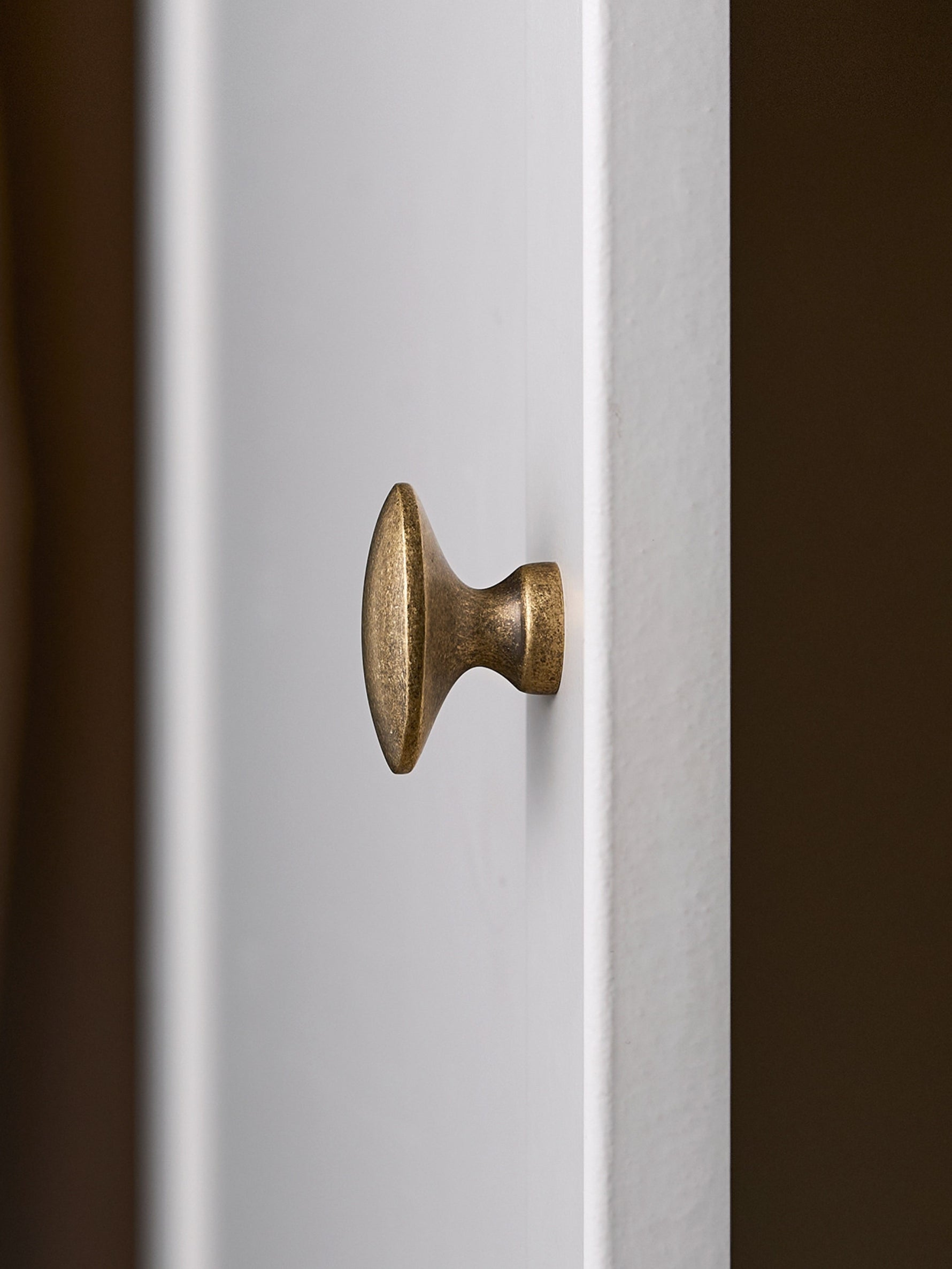 Antique brass oval cabinet knob on white door, profile view showing pedestal