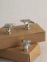 Three polished chrome star cabinet knobs displayed on stacked kraft boxes