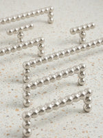 Four polished chrome beaded ball pulls scattered on speckled terrazzo surface showing size range