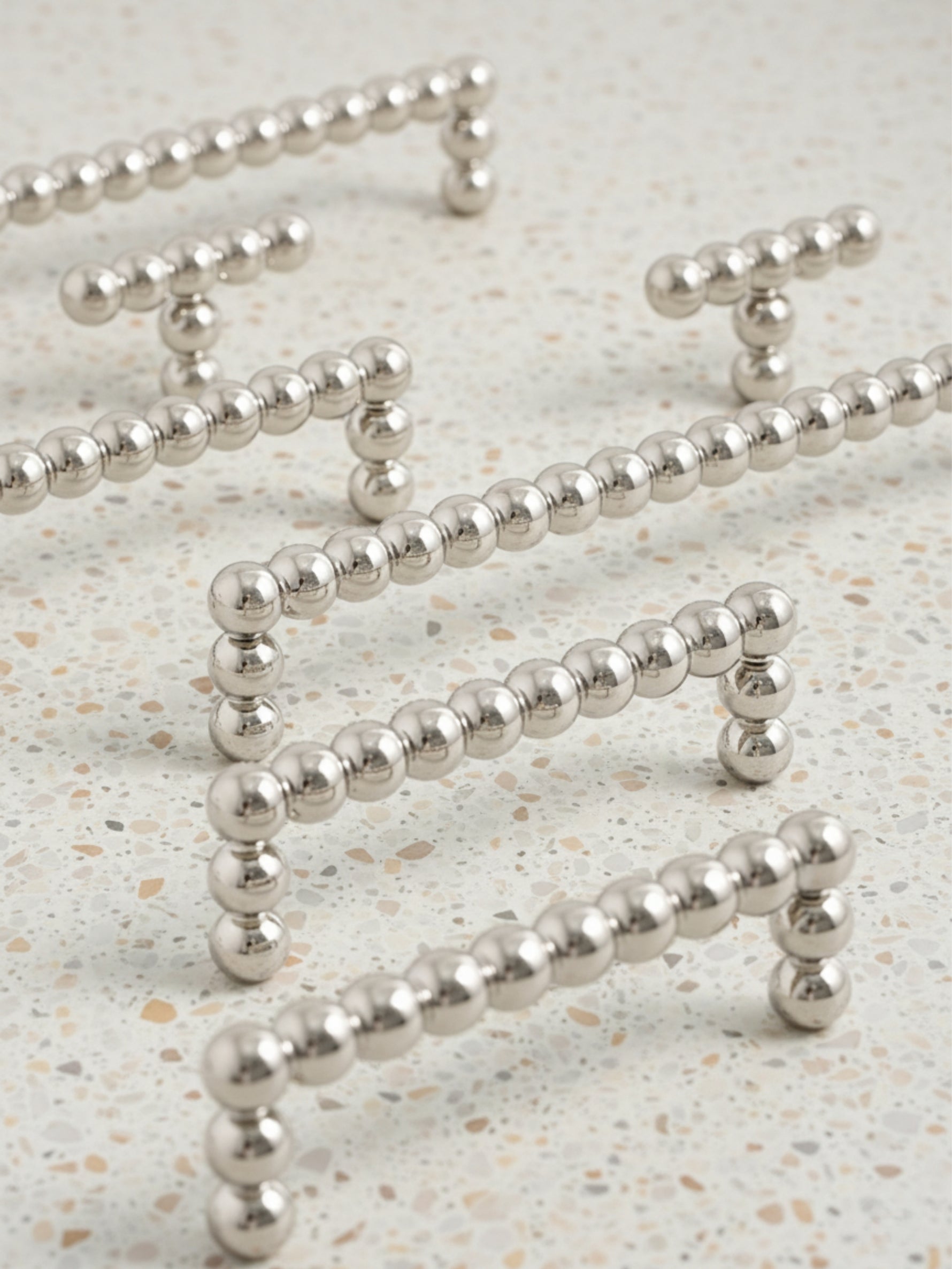 Four polished chrome beaded ball pulls scattered on speckled terrazzo surface showing size range