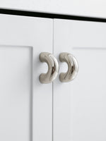 Two polished chrome arch knobs on white kitchen cabinet doors