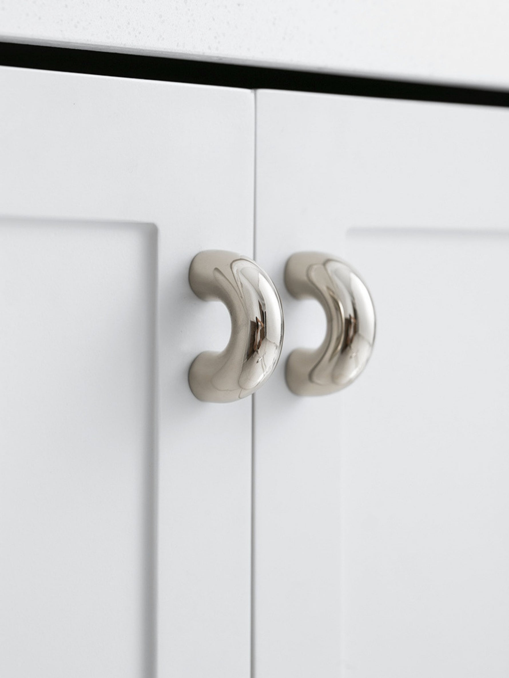 Two polished chrome arch knobs on white kitchen cabinet doors