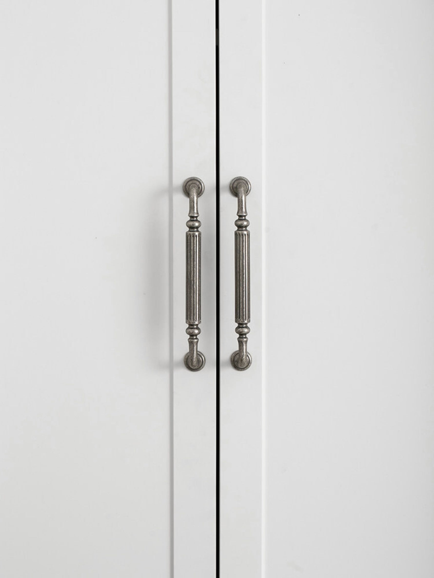 Two antique silver reeded pulls on white cabinet doors, front view