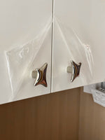 Polished chrome wave star knobs on white cabinet doors covered in plastic packaging film