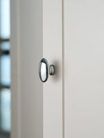 Polished chrome oval cabinet knob on white door, side profile view