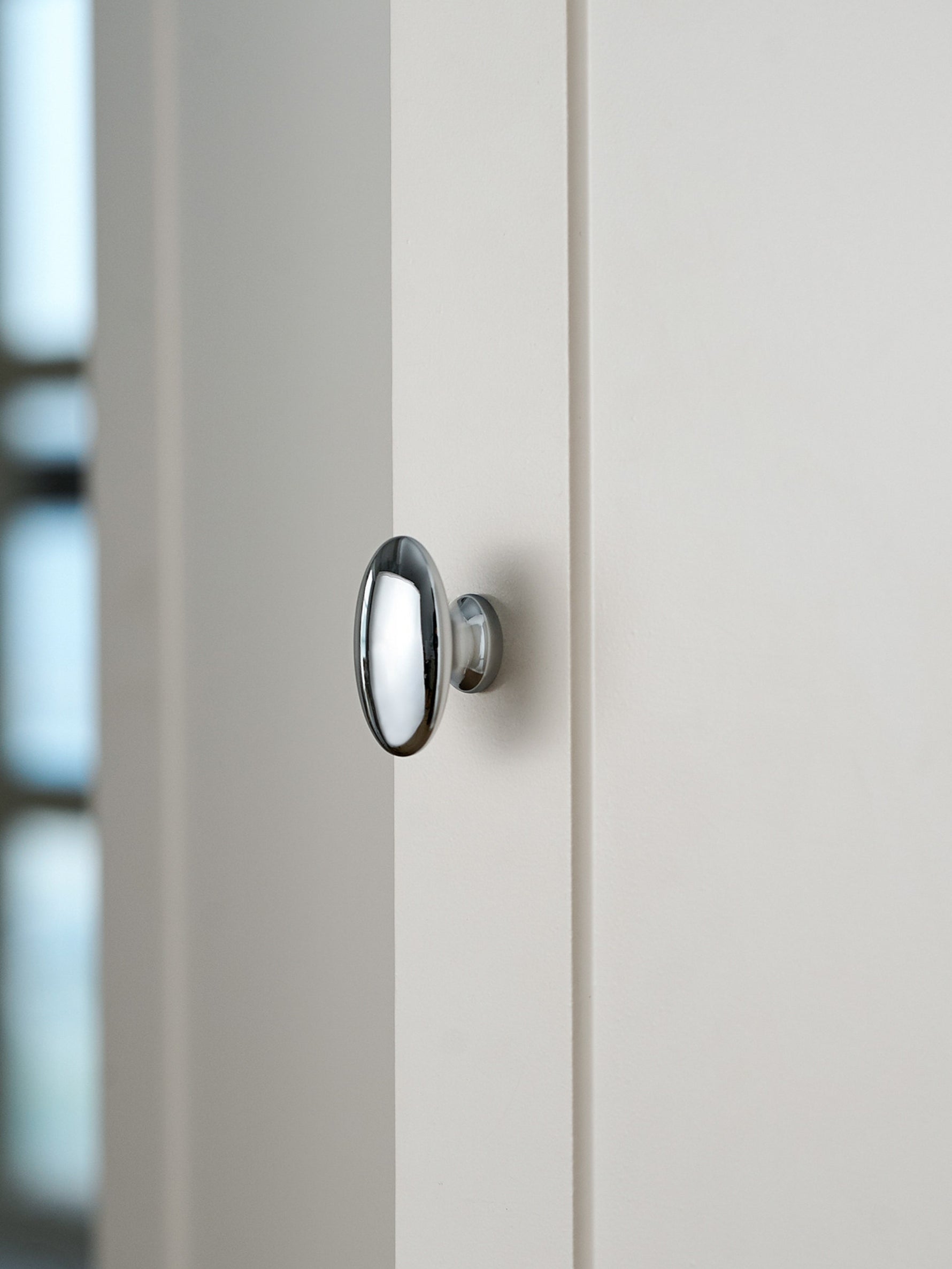 Polished chrome oval cabinet knob on white door, side profile view