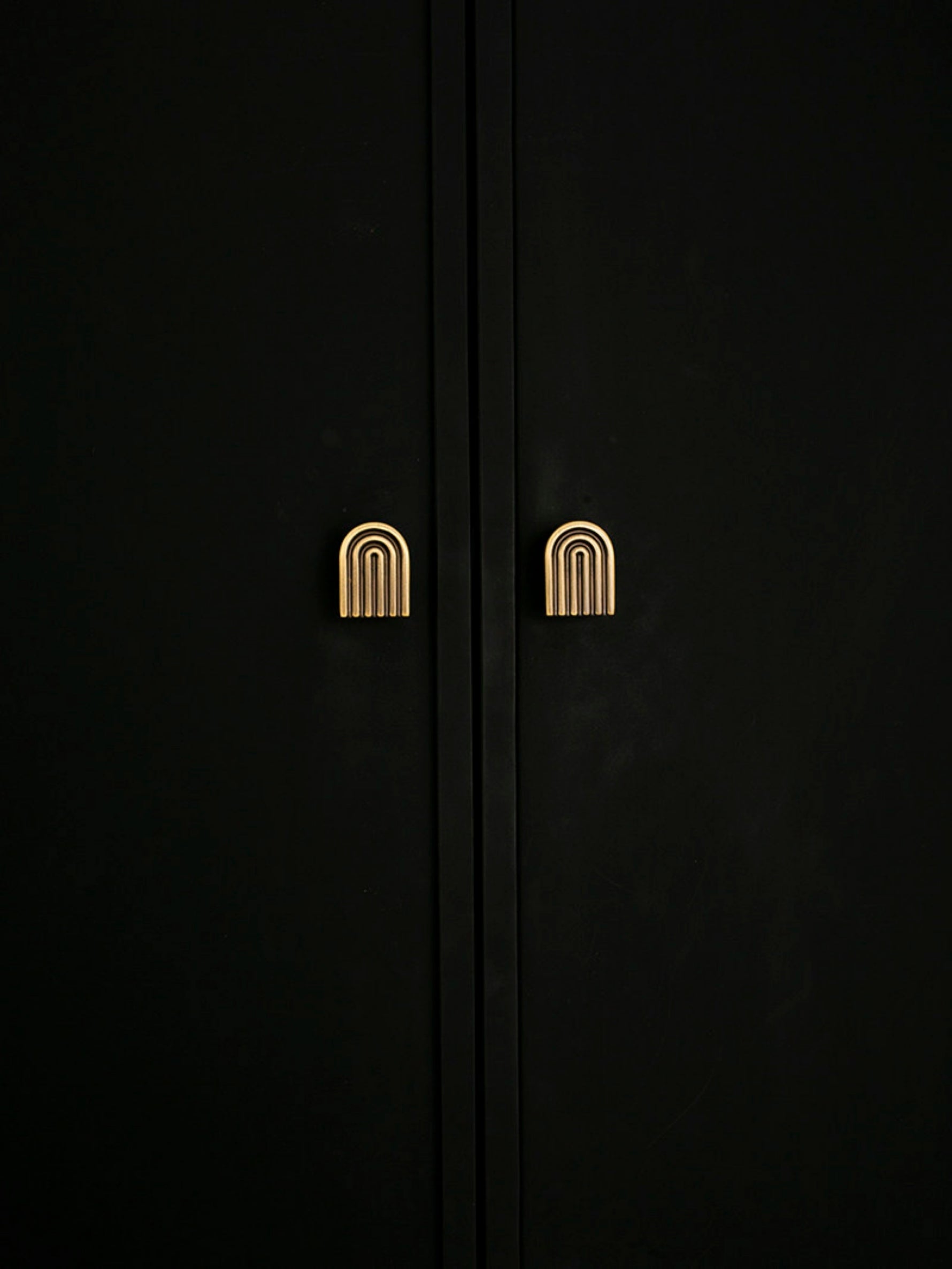 Pair of solid brass Art Deco arch knobs mounted on dark wardrobe doors