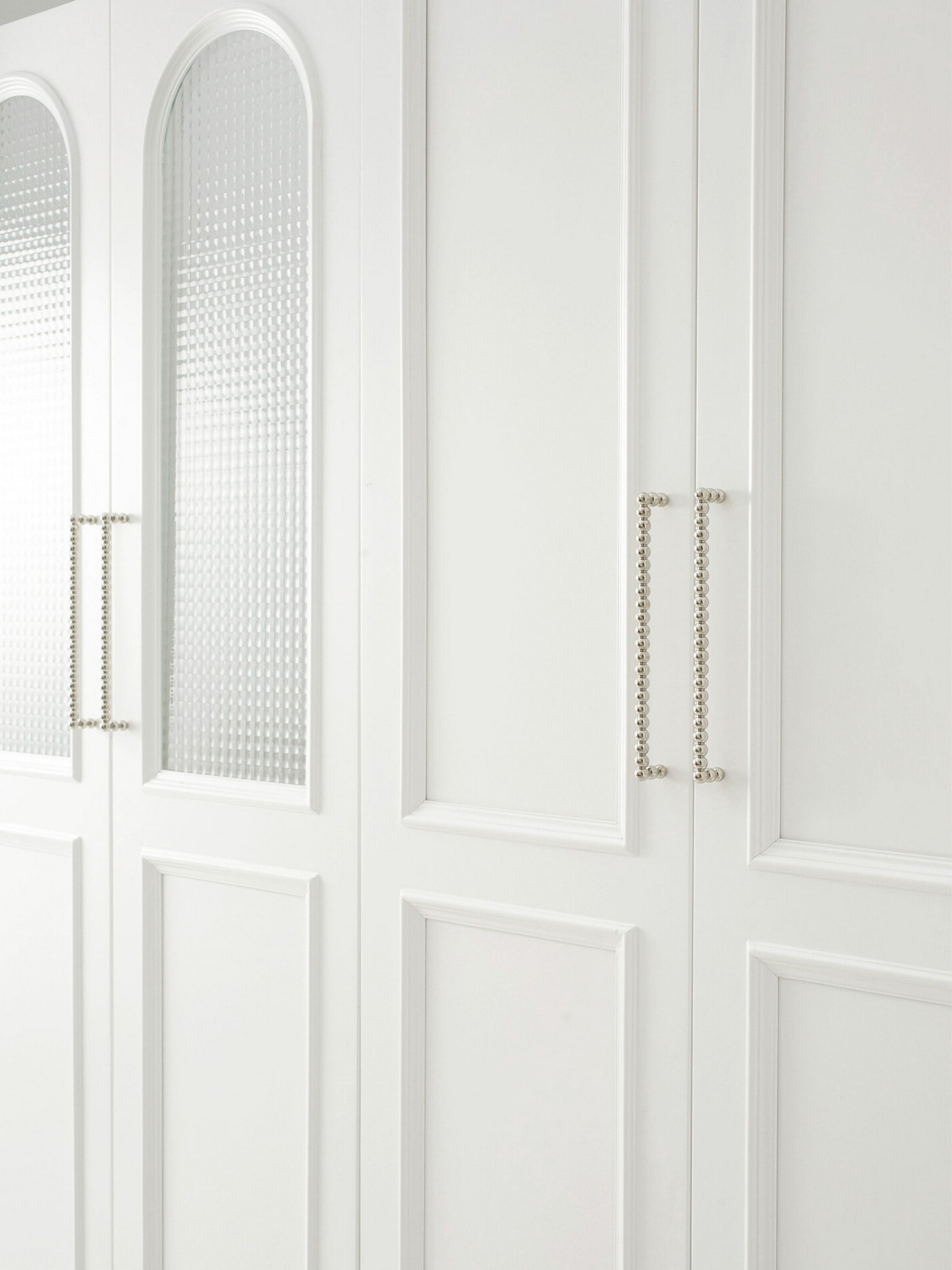 Two polished chrome beaded ball pulls on white fluted glass wardrobe doors