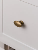 Antique brass oval knob on cream drawer front, close-up angled view