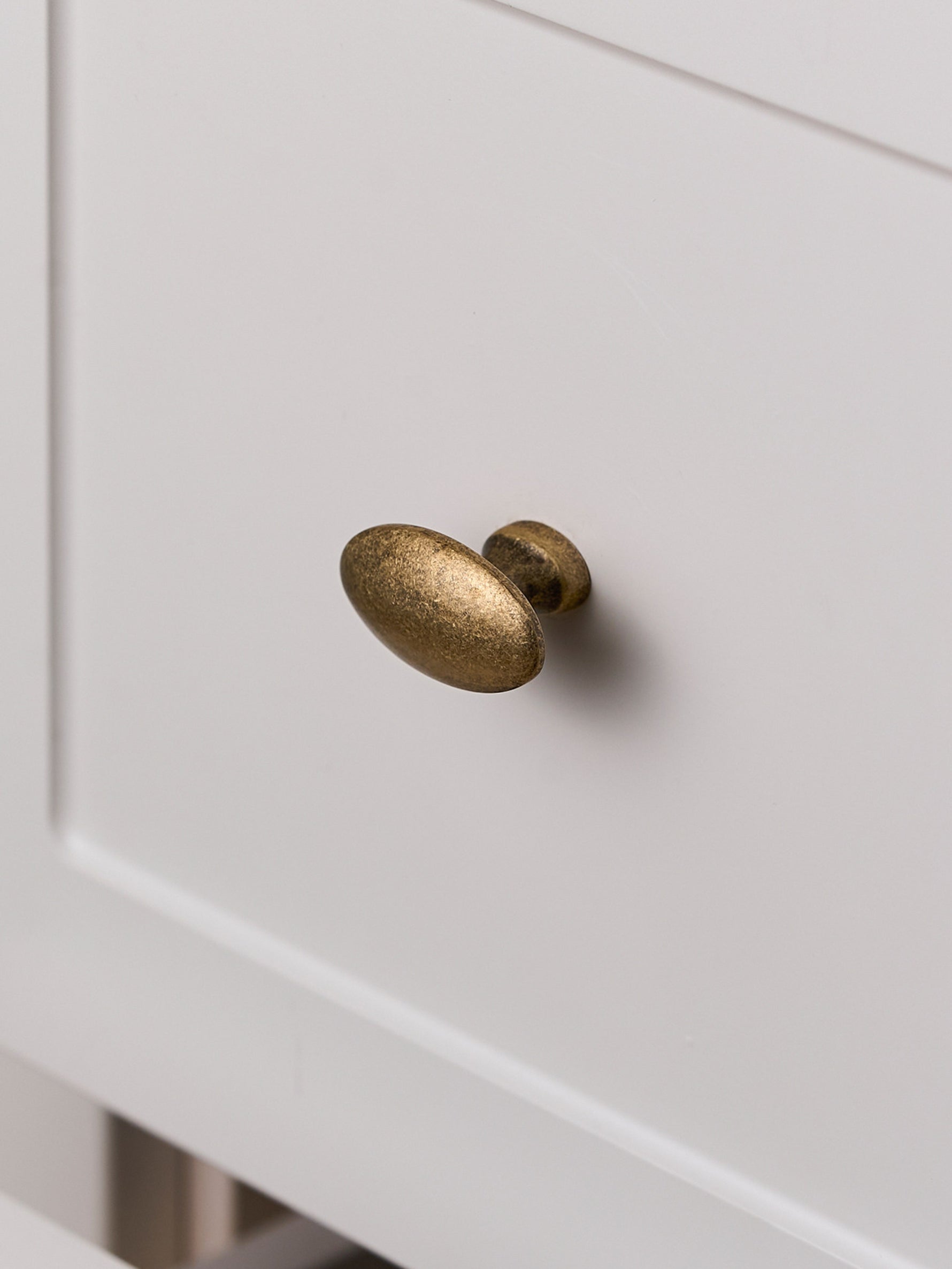 Antique brass oval knob on cream drawer front, close-up angled view