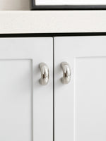 Two polished chrome arch knobs on white shaker cabinet doors with marble countertop