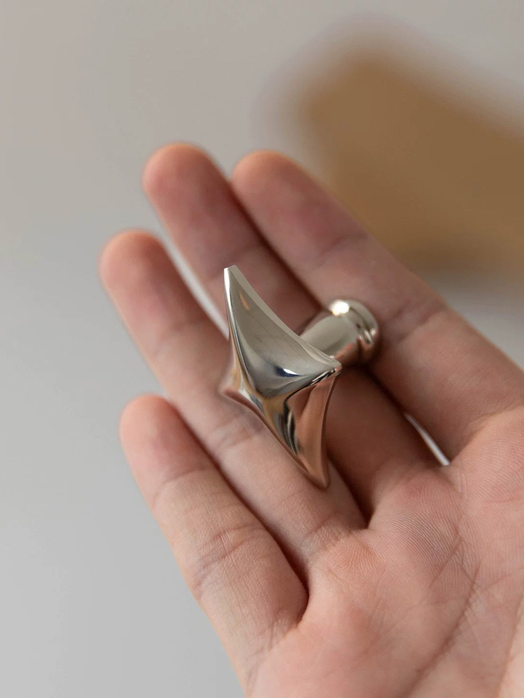 Polished chrome star cabinet knob held in open palm, close-up