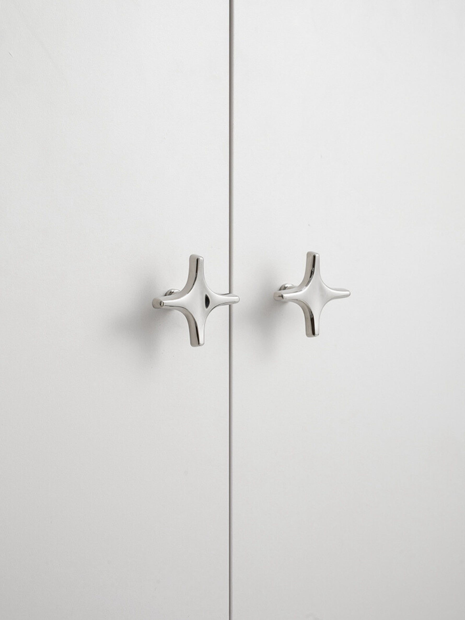 Close-up polished chrome star knobs on white cabinet doors