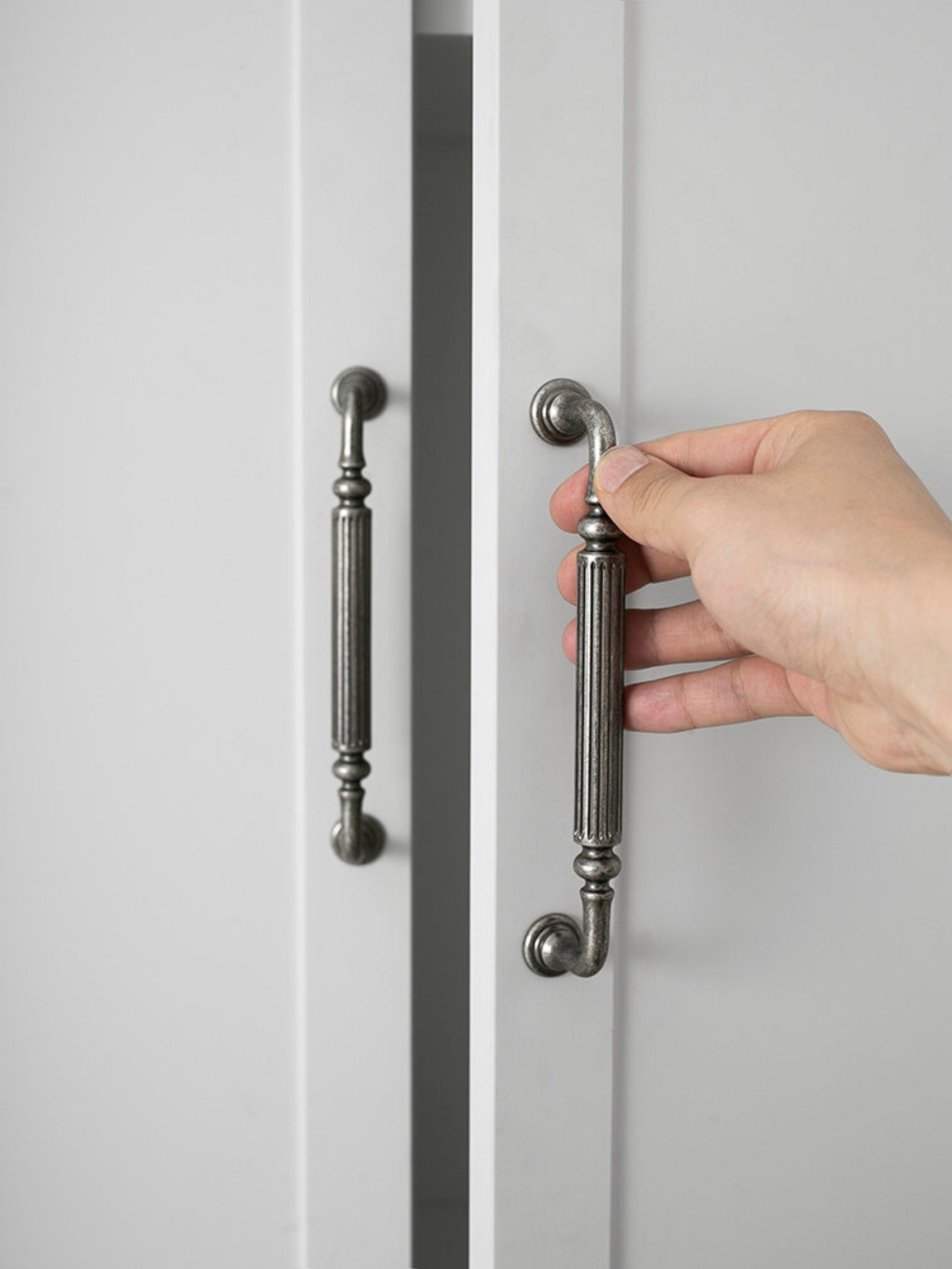 Hand gripping antique silver reeded cabinet pull on white door
