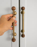 Hand holding antique brass walnut ball pull on white wardrobe