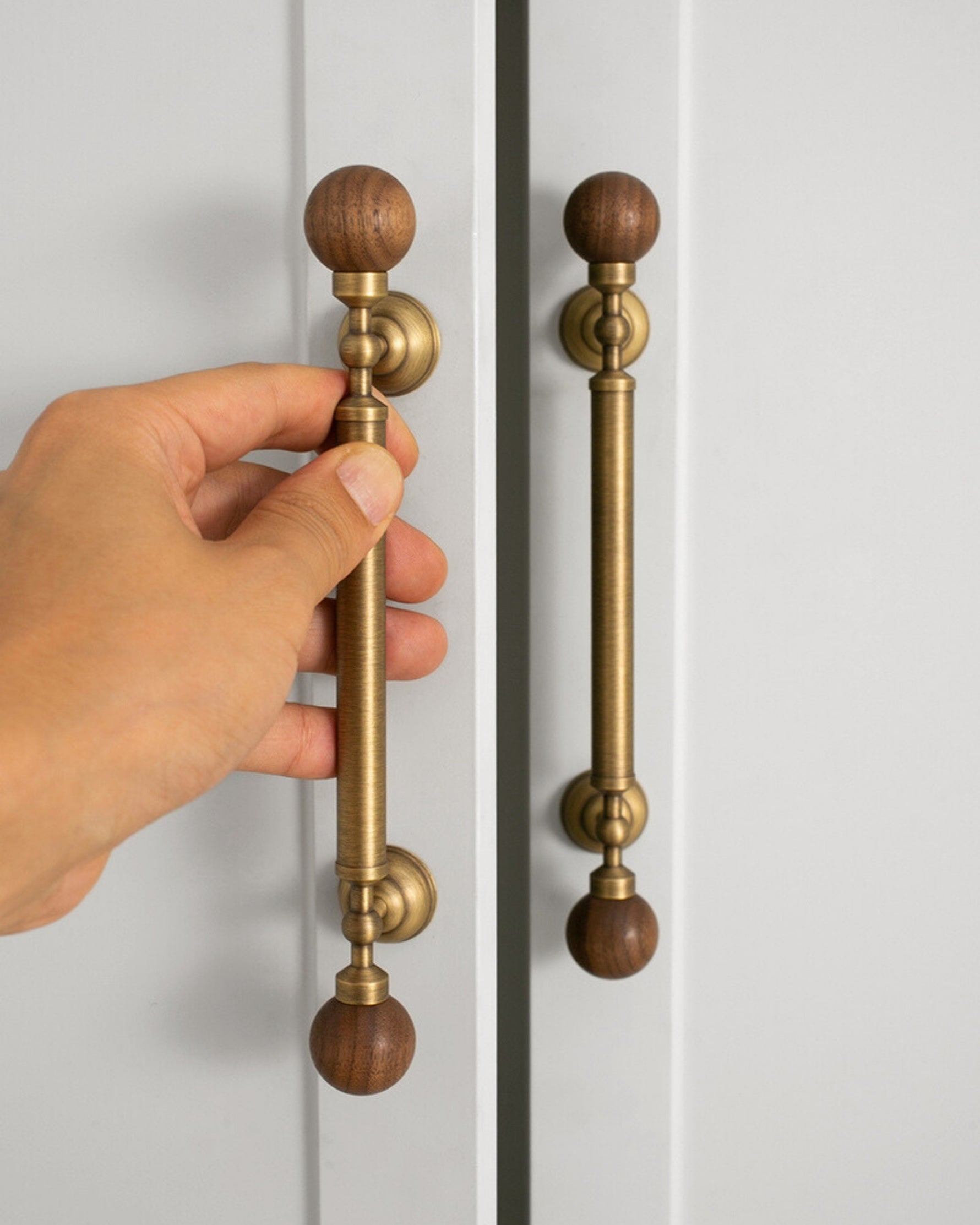 Hand holding antique brass walnut ball pull on white wardrobe