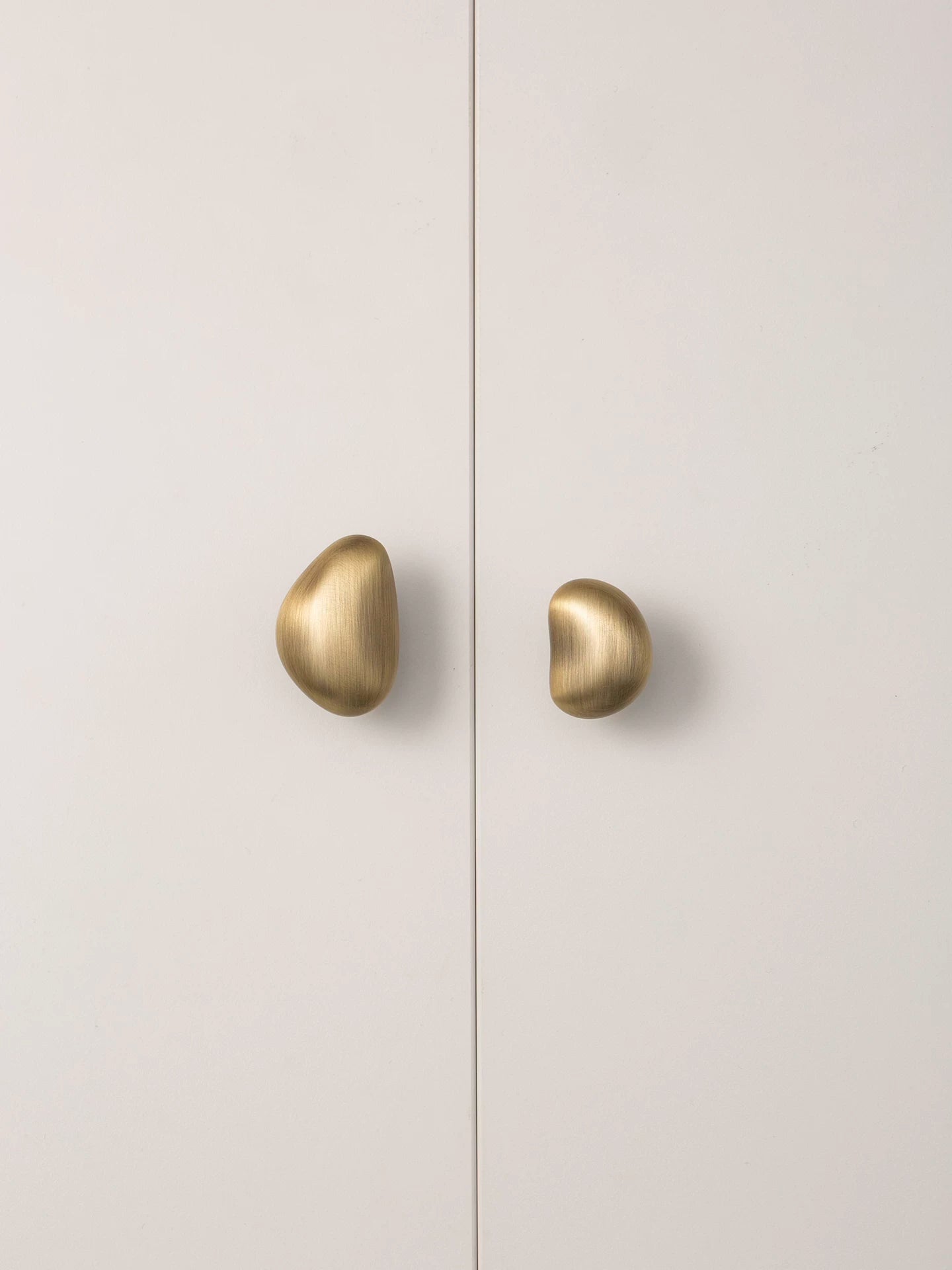 Brushed brass pebble cabinet knobs on white wardrobe door