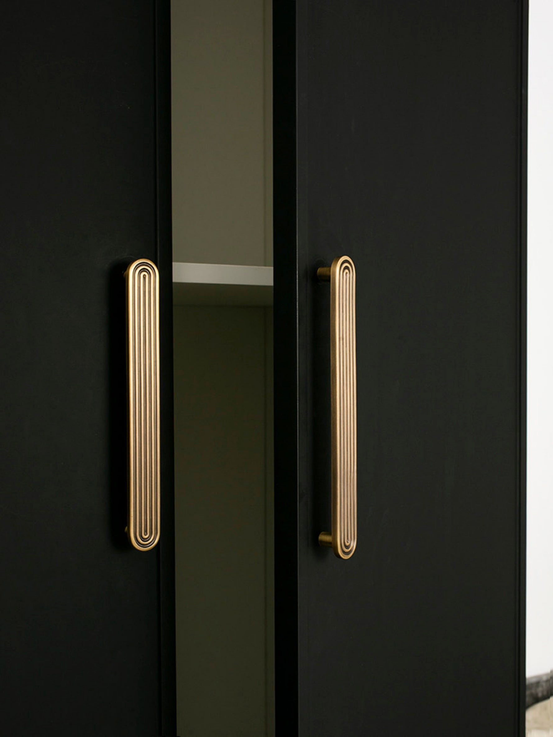 Tall solid brass Art Deco arch door pull on black wardrobe — vertical orientation
