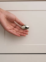 Nickel silver oval cabinet knob held in open palm against white cabinet