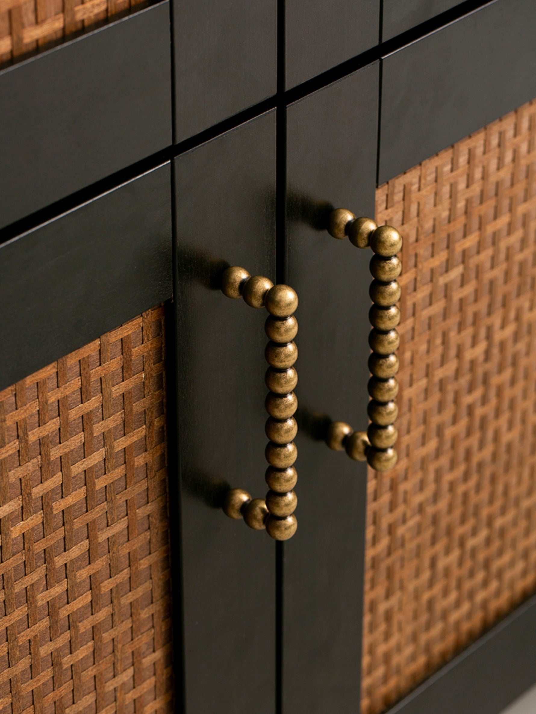 Close-up of a cabinet with black and brown wicker design and antique brass handle.