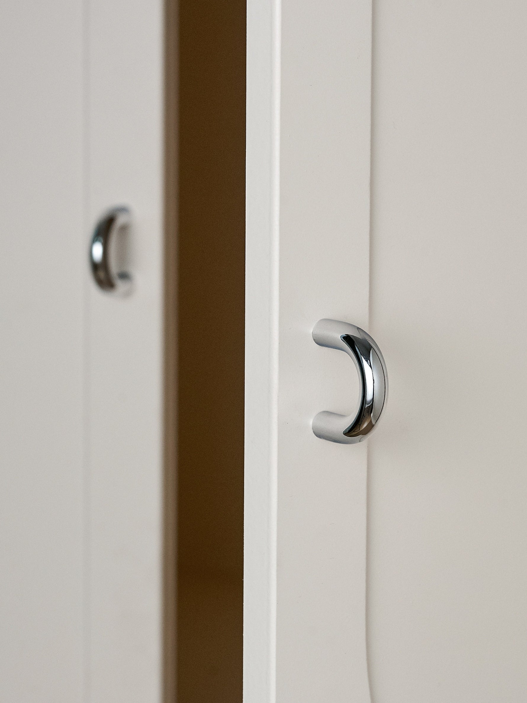 Two polished chrome cup pulls on white cabinet doors, close-up